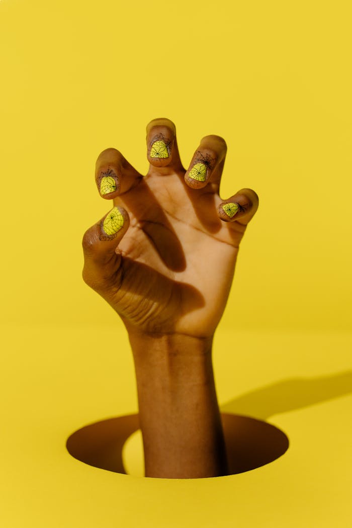 A creatively styled hand with yellow cracked nail polish emerging from a hole in a yellow background.